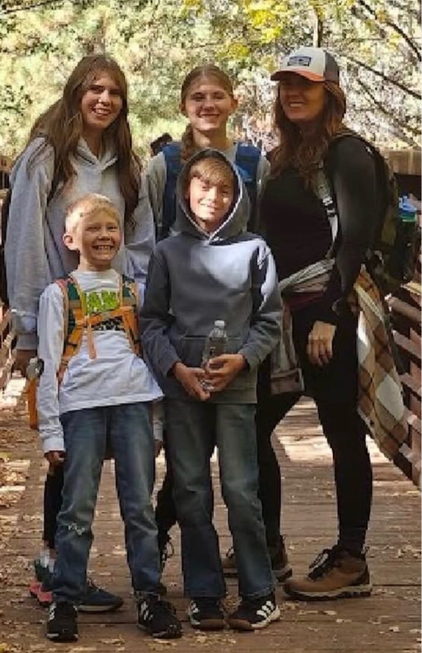 Lori Pappin and family walking across a wooden trail bridge in the forest